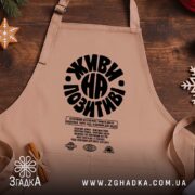 Фартух живи на позитиві, бежевий, на дерев'яному фоні, бренд Згадка.