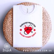 Футболка медсестра золотий стандарт, біла, на кошику, вид зверху, бренд Згадка.