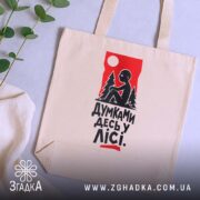Шопер думками десь у лісі, бежевий, з принтом, на фоні рослин, бренд.