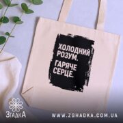 Шопер холодний розум на столі, бежевий з чорним принтом, зелень на фоні,.