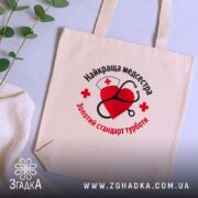 Шопер медсестра золотий стандарт, бежевий, на столі, зелена рослина, бренд Згадка.