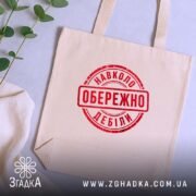 Шопер обережно навколо дебіли, бежевий, зверху, на фоні рослин, бренд Згадка.
