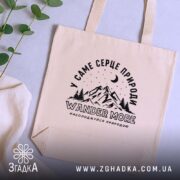 Шопер wander more для любителів гір, бежевий, на столі, з рослинами, бренд.