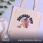 Шопер зіпсована фея, бежевий, на столі з рослинами, принт феї, бренд Згадка.