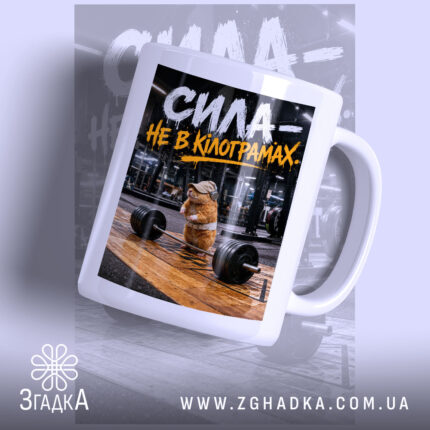 Чашка сила не в кілограмах, біла чашка з принтом, ручка зліва, фон.