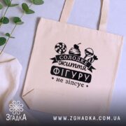 Шопер солодке життя фігуру не зіпсує, бежевий, на столі, з рослинами, текстура.