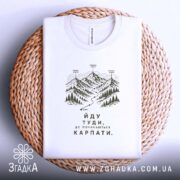 Футболка йду туди де починаються Карпати, біла, на столі, складена, бренд Згадка.