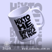 Біла чашка з чорним написом у похилому ракурсі, ручка праворуч.