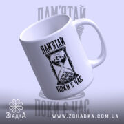 Біла чашка з написом «Пам’ятай поки є час» у похилому ракурсі, ручка праворуч.