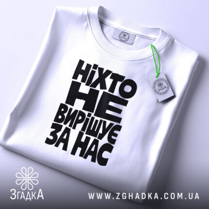 Складена біла футболка з чорним типографічним принтом, ракурс під кутом.