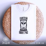 Складена футболка з написом «Пам’ятай поки є час» на плетеній поверхні.